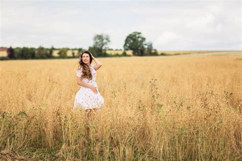 A Brunette Woman In A White Dress Runs Along A Field Stock Photo