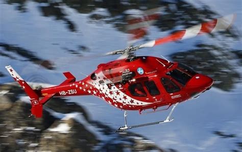 a red helicopter flying through the air over snow covered mountains