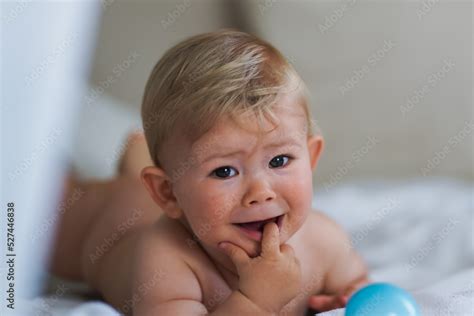 Sad Naked Almost One Year Old Blond Baby Boy Lying At Home On A Cozy Bed After Bathing In Prone