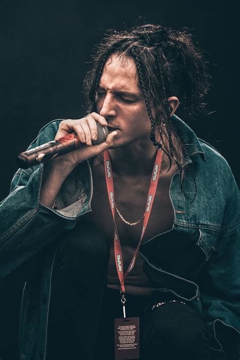 A Man With Dreadlocks Is Holding A Microphone To His Mouth And Looking Down