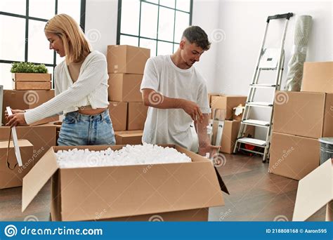 Young Caucasian Couple Smiling Happy Unboxing Cardboard Box At New Home