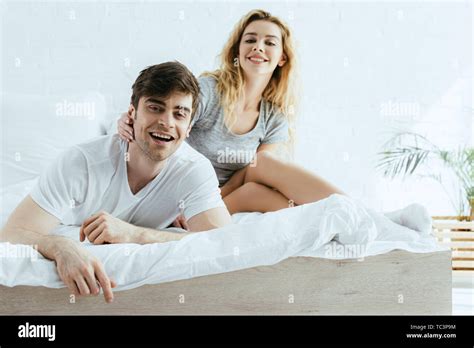 Cheerful Blonde Girl Touching Happy Man Lying On Bed Stock Photo Alamy