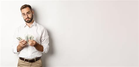 Красивый бизнесмен считает деньги и смотрит в камеру, серьезно стоя на ...