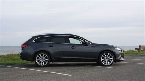 A Black Car Parked In A Parking Lot Next To The Ocean With Grass On