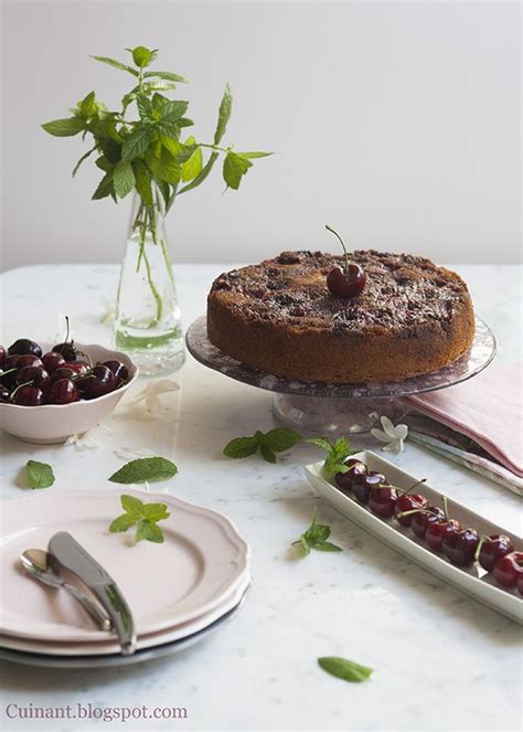 A Table Topped With Plates And Cake Next To A Vase Filled With Cherries