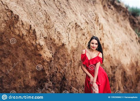 Mujer Hermosa En El Vestido Rojo Que Presenta En Fondo Del Acantilado