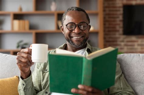 Heureux Homme Noir Mature Dans Des Verres Apprécie Une Tasse De Café Et Lit Un Livre Pendant Son