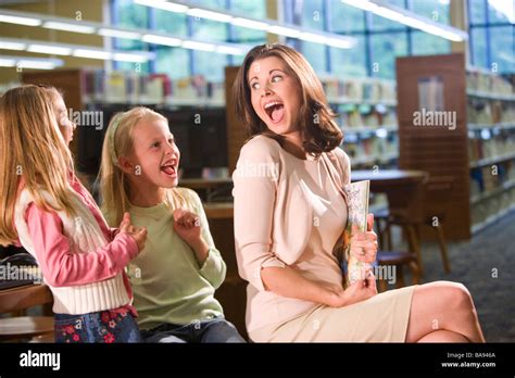 Elementary School Teacher Laughing With Girls In Library Stock Photo