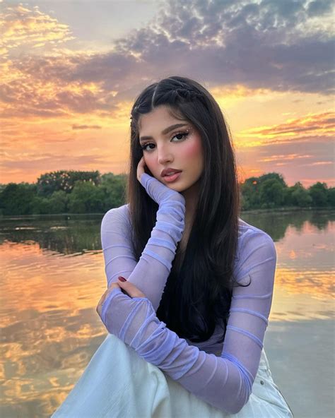 A Woman Sitting On The Edge Of A Body Of Water With Her Hand Under Her Chin