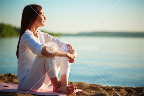 Side View Of Serene Woman Sitting On Sandy Beach Against Blue Sky