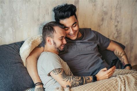 Pares Gay Felices Que Mienten Junto En Cama Y Que Usan El Smartphone Mirando Las Fotos Foto De