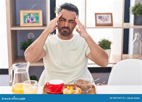 Hispanic Man With Beard Eating Breakfast With Hand On Head Headache Because Stress Stock Image