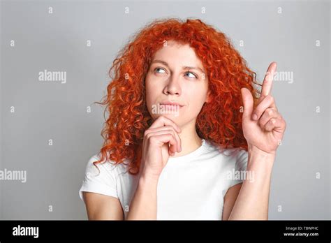 Thoughtful Redhead Woman With Raised Index Finger On Grey Background