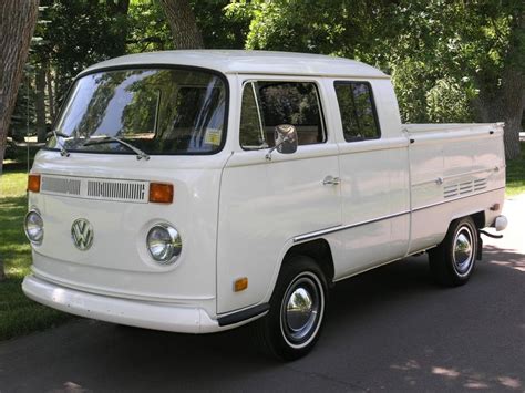 An Old White Vw Bus Parked On The Side Of The Road In Front Of Some Trees