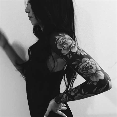 A Woman With Long Black Hair And Tattoos On Her Arms Is Standing In