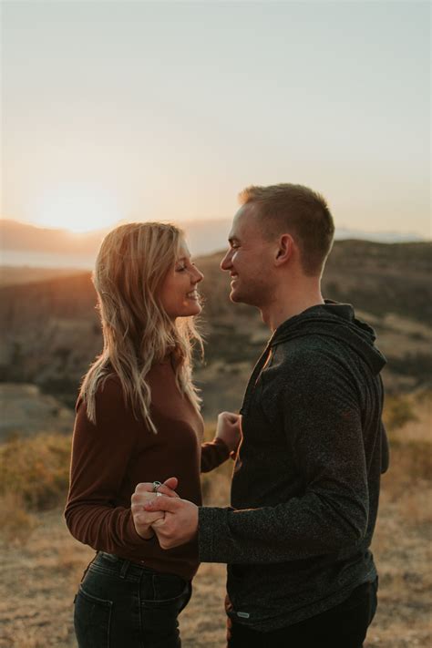 A Man And Woman Standing In The Desert At Sunset With Their Arms Around