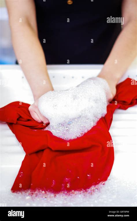 Closeup womans hands handwashing clothes in red plastic washbucket ...