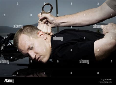 Man Being Handcuffed By Police Officer On Hood Of Black Car Stock Photo