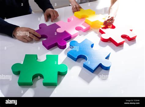 Two Businesspeople Solving Multi Colored Jigsaw Puzzle Over White Desk