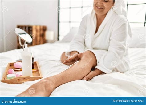 Middle Age Grey Haired Woman Caring Skin Legs Using Hydration Cream Sitting On The Bed At