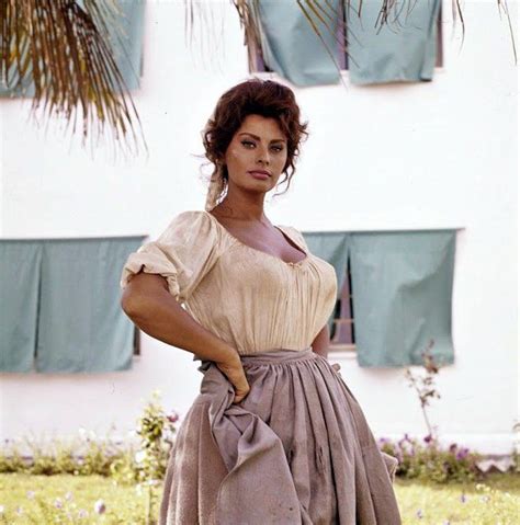 A Woman Standing In Front Of A Building Wearing A Dress And Holding Her