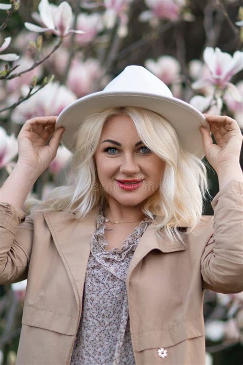 Magnolia Flowers Woman A Blonde Woman Wearing A White Hat Stands In Front Of A Tree With Pink