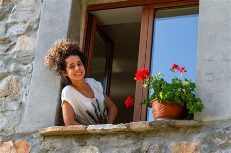 Atractiva mujer joven asomándose por una ventana con flores Foto Premium