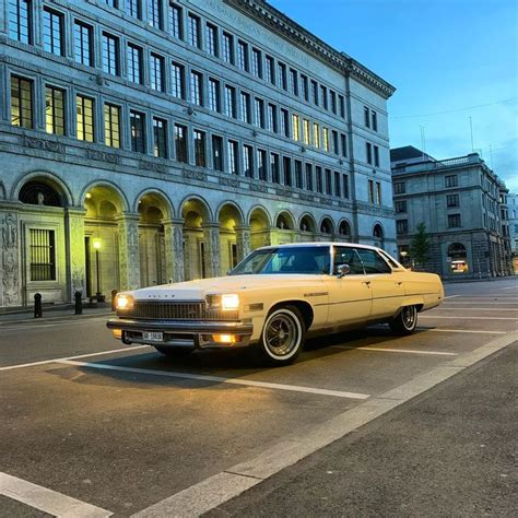 an old car is parked in front of a large building at night with its ...