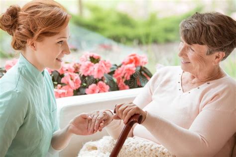 Smiling Caregiver Supporting Happy Senior Woman With Walking Sti Stock