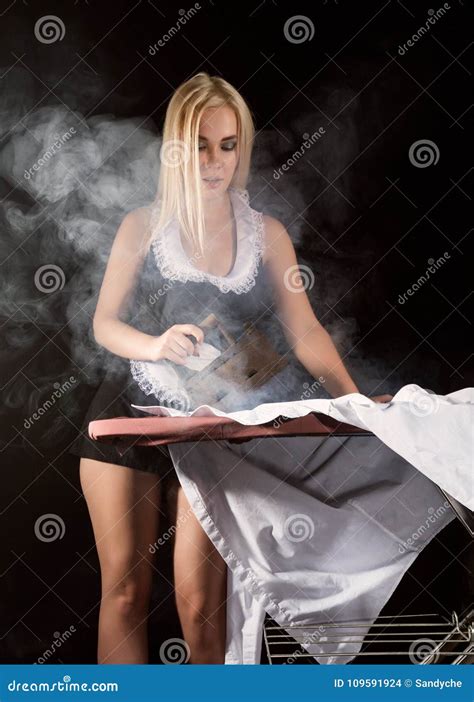 Blonde Woman In Housekeeper Suit Ironing White Shirt With Old Iron Retro Style On A Dark