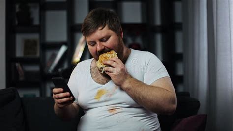 Dirty Fat Bearded Man Talks On The Smartphone Eating A Burger And