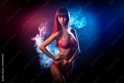 Beautiful Woman With Dark Long Hair In Red Lingerie Looks At The Camera And Posing Against A