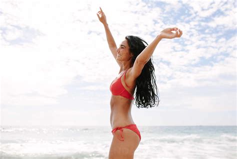 Mujer joven en bikini bailando en la playa Modelo femenina caucásica en la orilla del mar