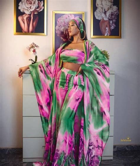 A Woman In A Pink And Green Dress Standing Next To Two Pictures On The Wall