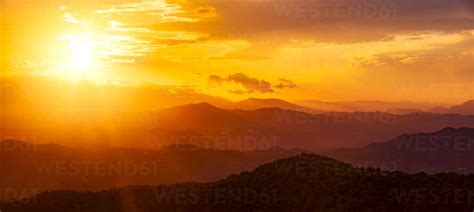 Dramatic orange sky over silhouette mountains in Montes de Malaga Natural Park at sunset ...