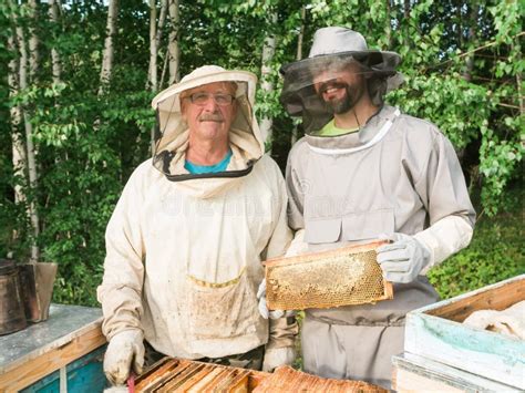 Portrait Of Two Male Beekeeper Working In An Apiary Near Beehives With