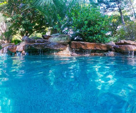 a pool with blue water and rocks in the middle is surrounded by greenery, shrubs and trees