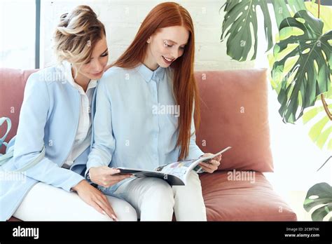 Redhead And Blonde Women Sit On Sofa And Enjoy Looking Journal Modern Fresh Stock Photo Alamy