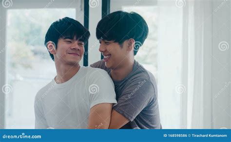 Una Coppia Gay Asiatica In Piedi E Abbracciandosi Vicino Alla Finestra Di Casa Giovani LGBTQ
