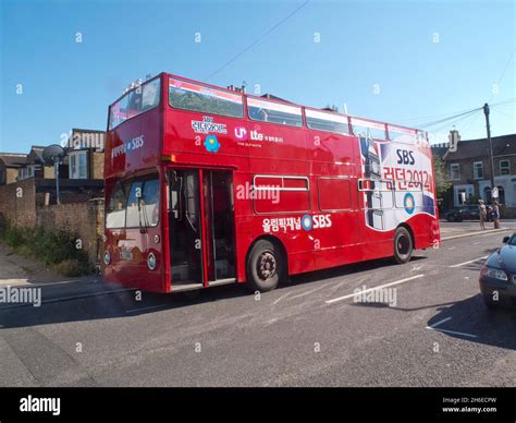 A Open Top Olympic Double Decker Bus Is Parked In A Surbuban Street In