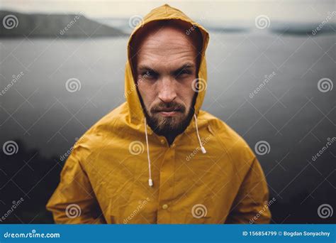 Brutal Bearded Man In Yellow Raincoat Standing On Cliff In Rainy Windy