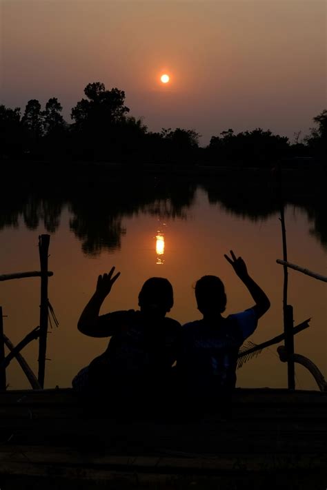 Silhouette of People Sitting Together and Posing on Lakeshore at Sunset ...