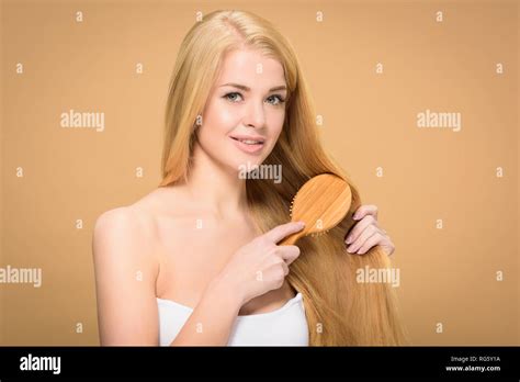 Happy Blonde Woman Brushing Long Hair On Golden Background Stock Photo