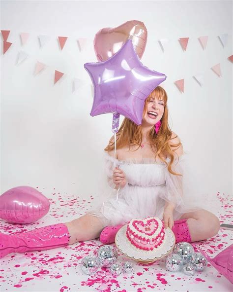 A Woman Sitting On The Floor With A Cake And Balloons In Front Of Her