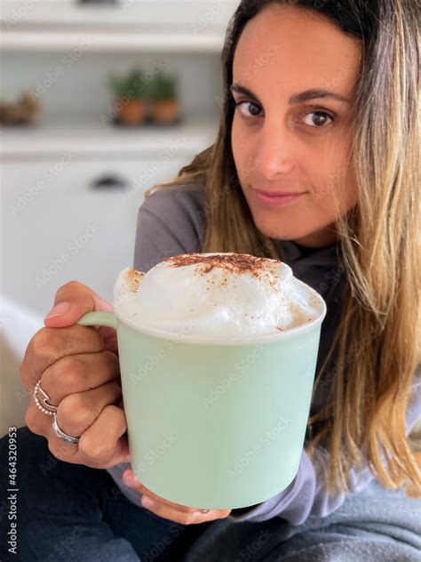 Niña latina tomando una taza de chocolate o café caliente y muy espumoso lleva poleron gris