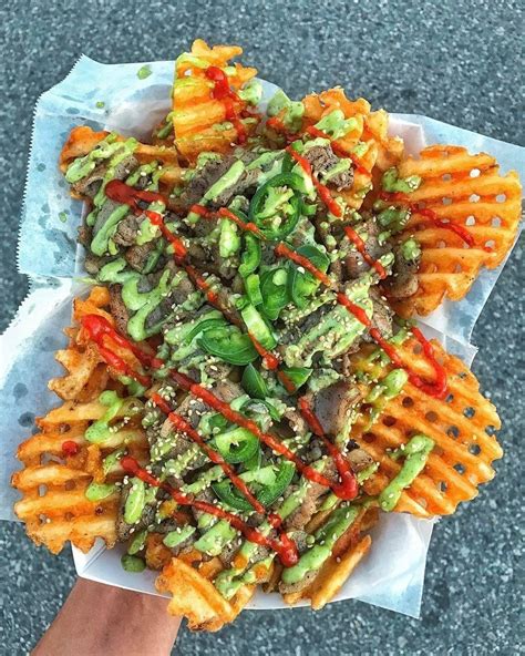 A Person Holding Up A Plate Of Food With Waffle Fries And Sauce On It