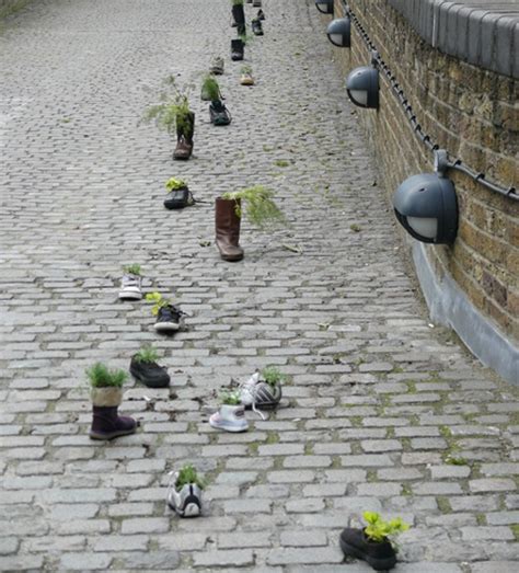 Many Potted Plants Are Growing On The Cobblestone Road Next To A Brick Wall