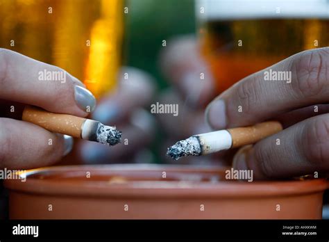 Two Hands Holding Cigarettes Into An Ashtray Stock Photo Alamy