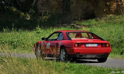 A Red Sports Car Driving Down A Road Next To Tall Grass And Trees In