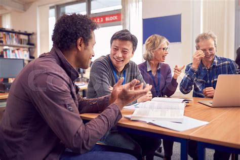 Teacher With Group Of Mature Adult Students In Class Sit Around Table And Work In College